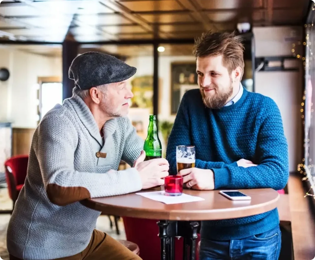 Two men talking and drinking at table.